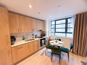 A modern kitchen with wooden cabinets, a dining table with chairs, and a window with curtains.