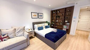 Een moderne slaapkamer met een bed, een slaapbank, een nachtkastje en een ingebouwde boekenkast.