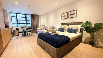 A modern hotel room with a large bed, a dining area, and a view of the city.