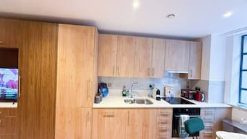 A modern kitchen with wooden cabinets, a sink, a stove, and a dining area with a green chair.