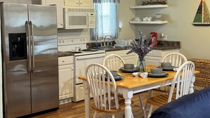 A compact kitchen with a refrigerator, microwave, and dining area with chairs and a table. - The Getaway @ Nolin  (Clarkson)