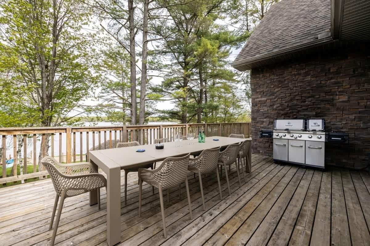 Une terrasse extérieure avec une table en bois et des chaises en osier, un mur en pierre et un barbecue encastré.