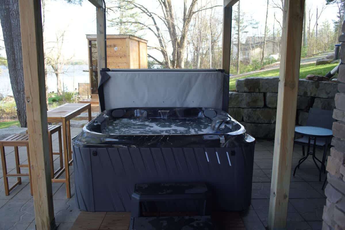 Ein Whirlpool mit Holzterrasse und Steinwand im Hintergrund, umgeben von Gartenmöbeln.