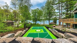 Un court de tennis entouré d’un paysage naturel, avec des arbres et une terrasse en bois.