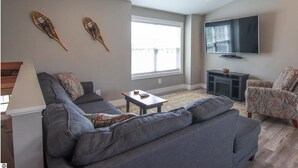 Ein modernes Wohnzimmer mit grauem Sofa, einem kleinen Tisch, einem Fernseher und Wanddekoration.