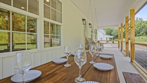 A covered patio with a wooden table set for dining, large windows, and a view of the outdoors. - Newly Built Home! 5 Minutes to Pigeon Forge! (Pigeon Forge)