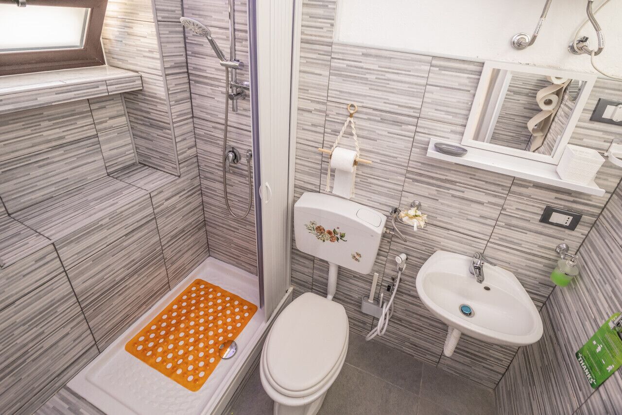 A bathroom with a shower, toilet, sink, and a small window.