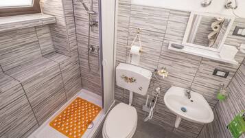 A bathroom with a shower, toilet, sink, and a small window.