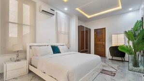 Une chambre à coucher moderne avec un lit blanc, une table de chevet, une armoire en bois et une plante en pot.