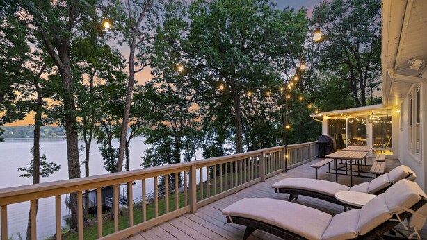 A wooden deck with lounge chairs and a covered area overlooking a lake, surrounded by trees.