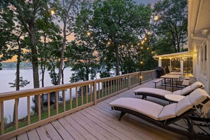 A wooden deck with lounge chairs and a covered area overlooking a lake, surrounded by trees.