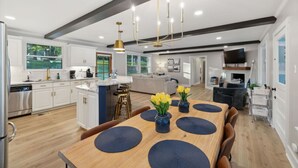 A modern kitchen with white cabinets, a wooden dining table with blue placemats, and a chandelier.