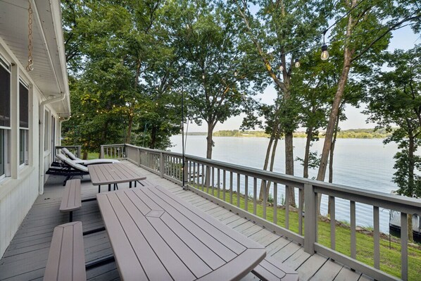 A wooden deck with picnic tables and a railing overlooking a lake.