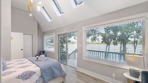 A bedroom with a bed, a nightstand, a lamp, and a view of a balcony with trees.