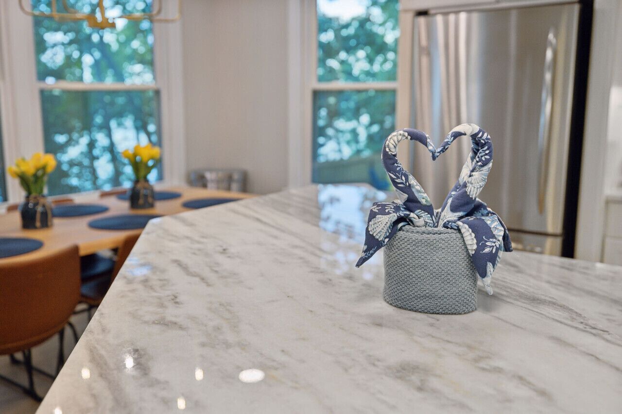 A kitchen with a marble countertop, a small knitted container with a heart-shaped design, and a view of trees through large windows.