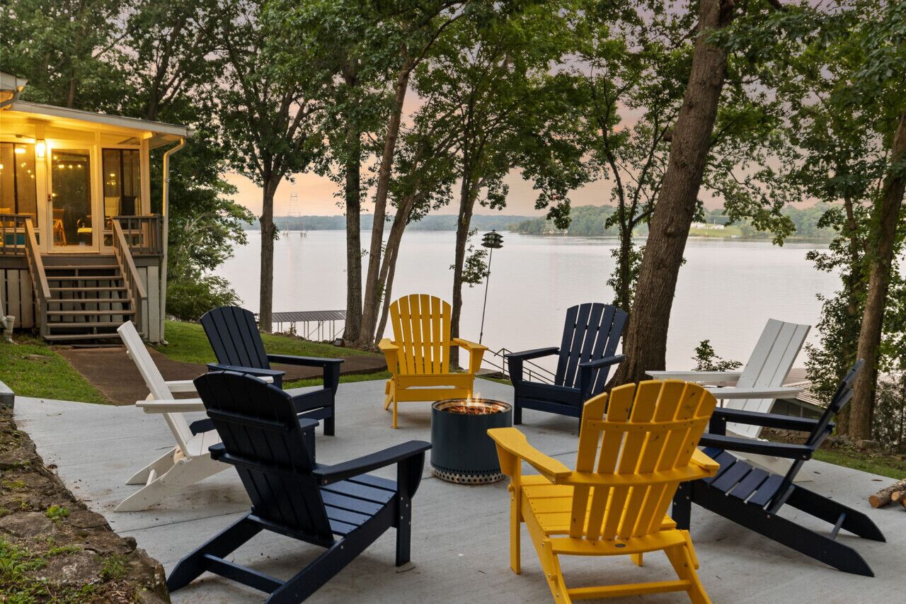 A lakeside deck with Adirondack chairs, a fire pit, and a covered seating area overlooking the water.