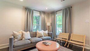 Una sala de estar con un sofá gris, dos sillones, una mesa redonda de centro y una lámpara.