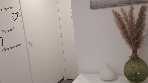 Un espace d’accueil avec un bureau blanc, un vase vert contenant des plumes d’herbe des pampas, un tableau représentant une plage et un tapis.