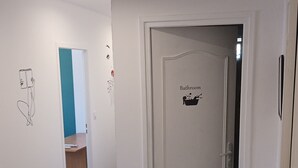 Un couloir avec une porte blanche sur laquelle est inscrit le mot « Salle de bain » et un petit tapis sur le sol.