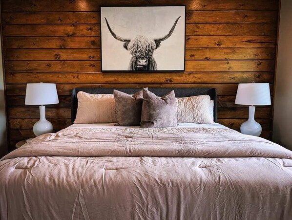 A bedroom with a wooden wall, a large bed with a patterned bedspread, and two bedside lamps.