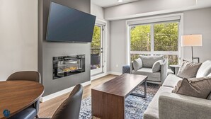 Una sala de estar moderna con televisor de pantalla plana, chimenea, sofá gris y comedor con mesa de madera.