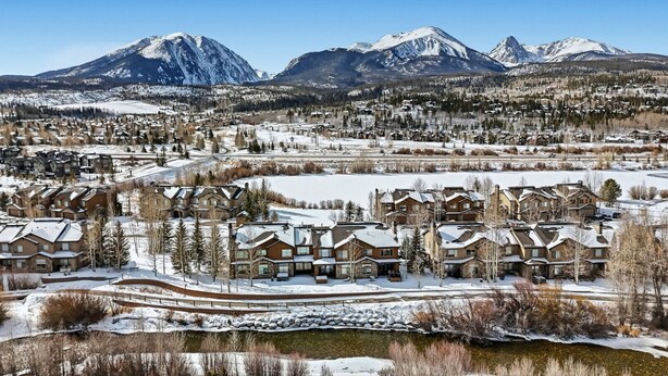 Una zona residencial cubierta de nieve con casas modernas, un telesilla y montañas al fondo.