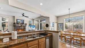 Cocina moderna con encimeras de granito, lavavajillas integrado y un comedor con sillas de madera y una araña.