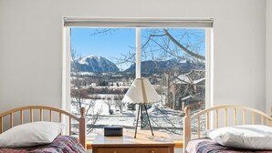 Un dormitorio con dos camas de madera, una mesita de noche, una lámpara y una ventana con vistas a la montaña.