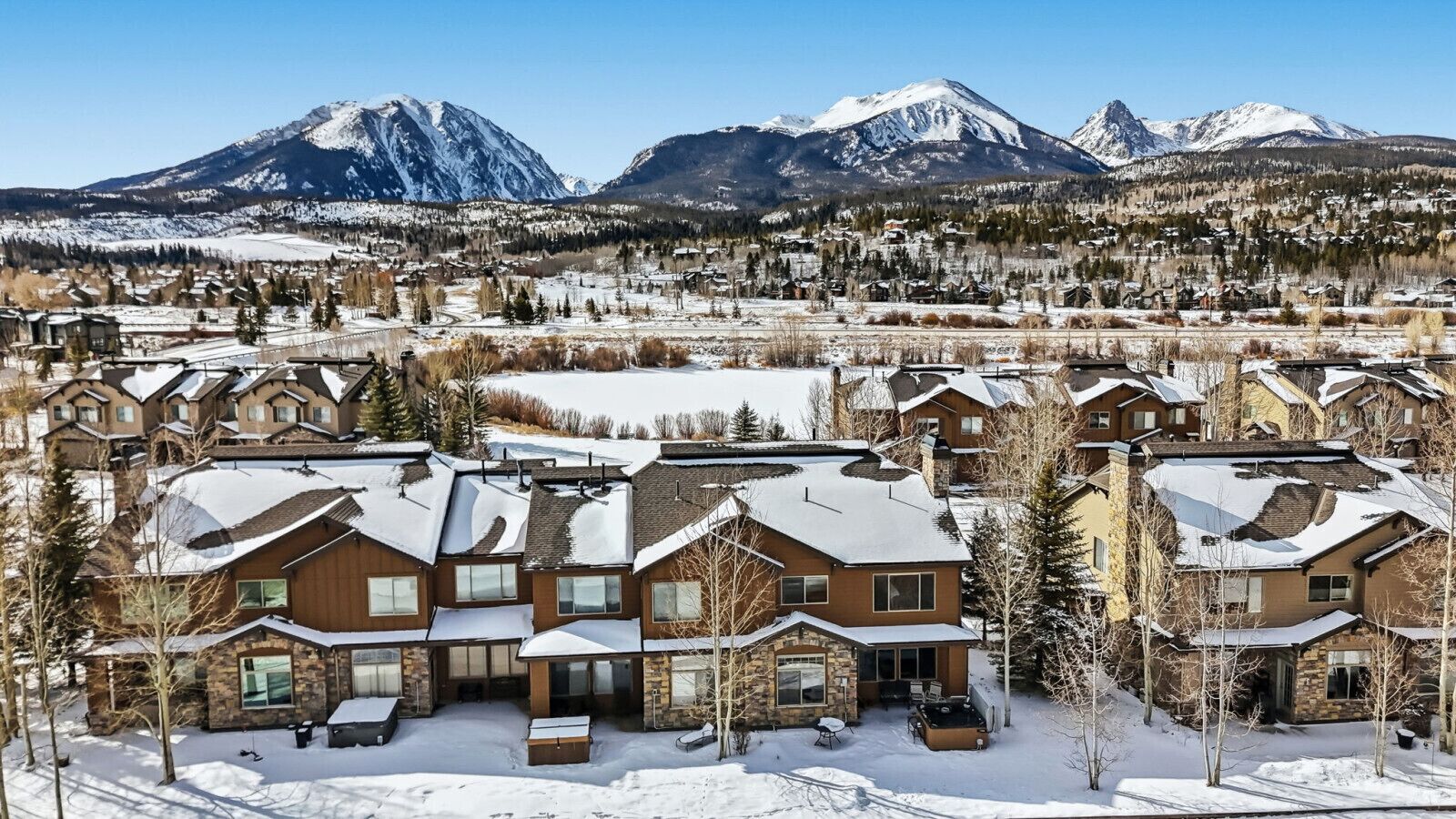A residential area with houses featuring sloped roofs and stone facades, surrounded by snow-covered mountains.