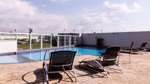 Un área de piscina en la azotea con cielos despejados, vistas de la ciudad y sillones de descanso.