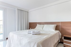 Un lit bien fait, avec une couette blanche et des oreillers, une tête de lit en bois et une fenêtre avec des rideaux.