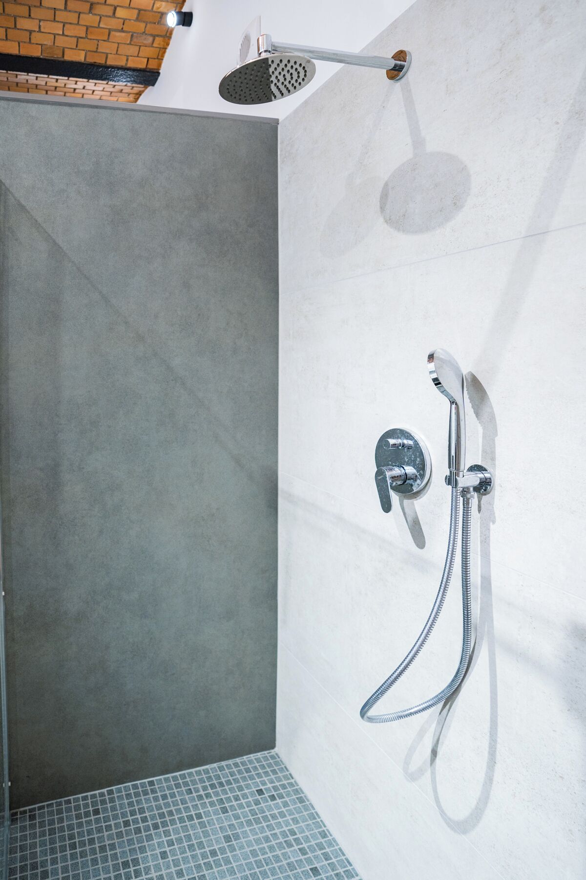 A shower area with a handheld showerhead and a wall-mounted faucet with a hose.