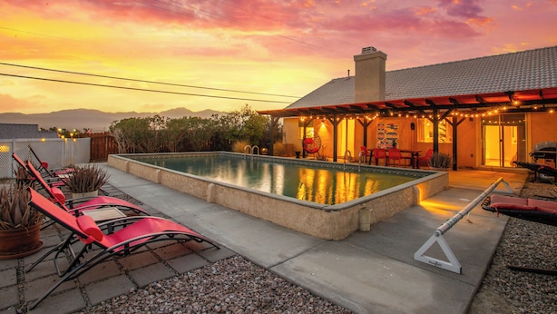 Ein Pool mit Liegestühlen, eine überdachte Terrasse und Blick auf die Berge.