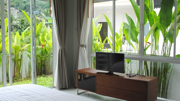 A bedroom with a large window, a bed, a TV on a wooden cabinet, and curtains.