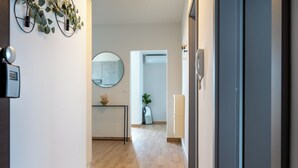 Un pasillo con piso de madera, un espejo redondo en la pared, una planta pequeña y una puerta que da a una habitación.