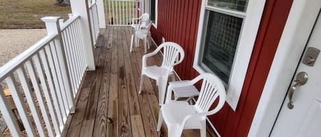 A wooden porch with white plastic chairs and a red exterior wall.