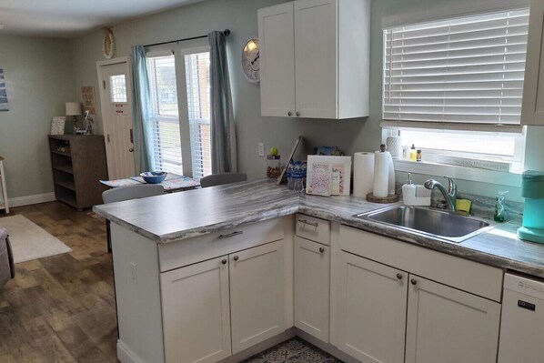 A compact kitchen with white cabinets, a marble countertop, a sink, and a window with blinds.