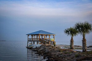 A wooden pier with a blue-roofed structure, palm trees, and calm water. - Pelicans Post - Close to Downtown & Beaches - King Bed - Boat Parking - NO Pet Fees ! (Port St. Joe)