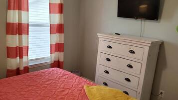 A bedroom with a bed, a dresser, a television on the wall, and a window with curtains.