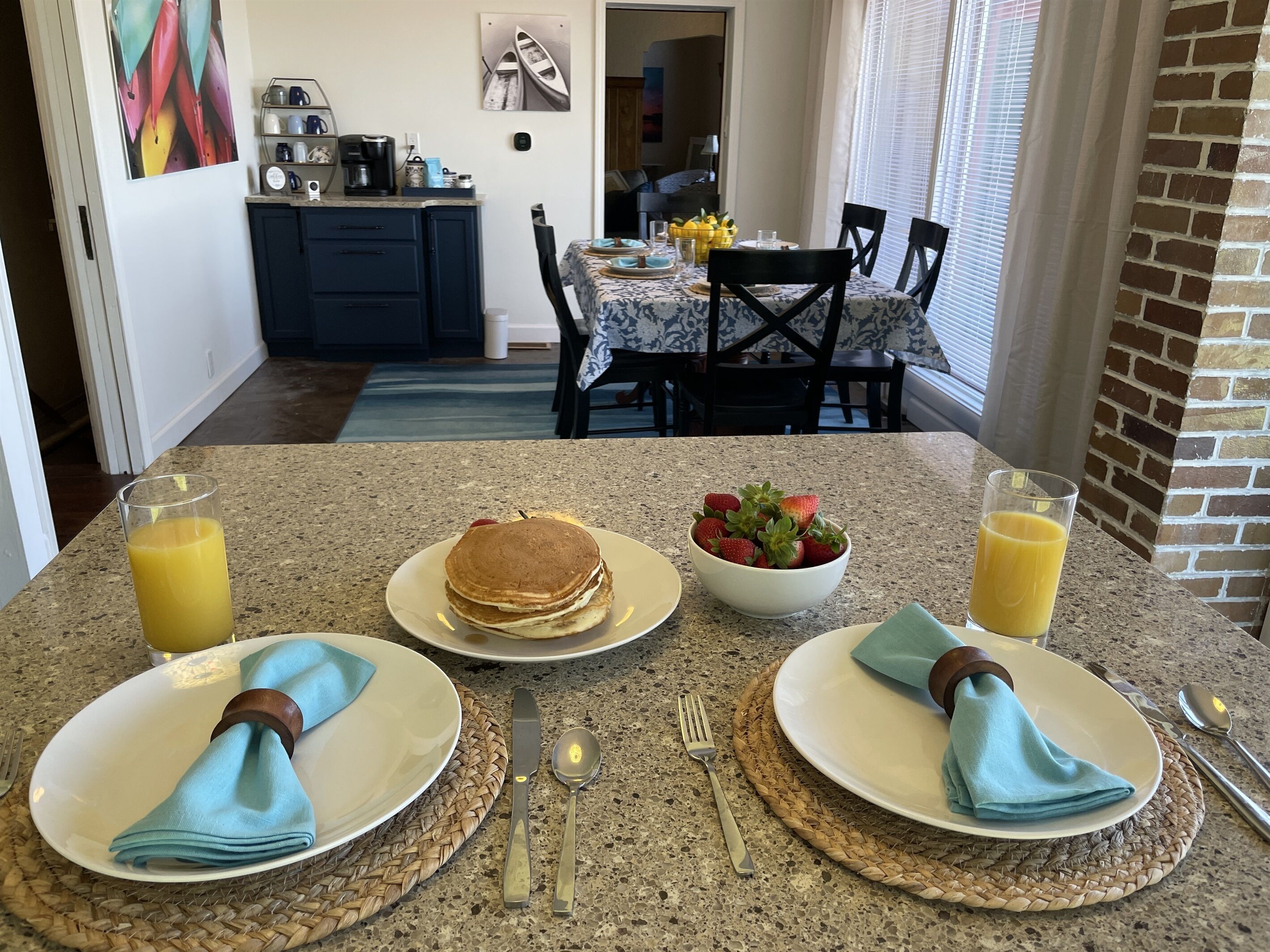 Une table mise pour le petit-déjeuner, avec des assiettes de crêpes, un bol de fraises et des verres de jus d’orange, le tout posé sur un comptoir en granit.