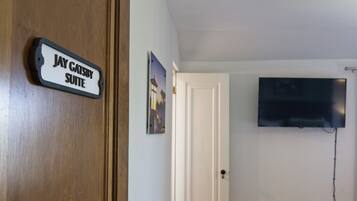 A room with a sign reading "Jay Gatsby Suite," a mounted TV, and a door.
