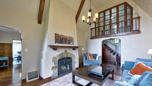 A spacious living room with a stone fireplace, wooden beams, a staircase, and a blue sofa.