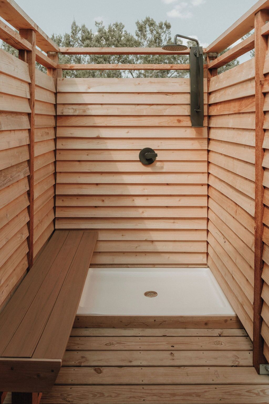 A wooden outdoor shower with a bench, surrounded by wooden walls.