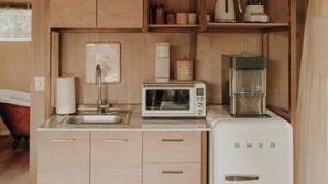 A compact kitchen with wooden cabinets, a microwave, a coffee maker, and a refrigerator. - Lavender - Luxury Glamping Tent (Johnson City)