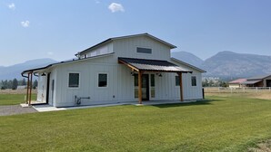 Uma casa branca de dois andares com varanda coberta e um amplo jardim frontal.