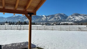 Um pavilhão de madeira com vista para montanhas cobertas de neve e um campo cercado.