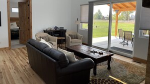 Uma sala de estar moderna com sofá, cadeiras, mesa de centro e vista para o exterior através de grandes portas de vidro deslizantes.