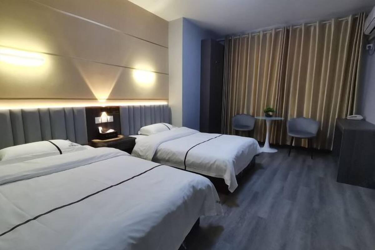 A hotel room with two beds, a desk, a chair, and a curtain.
