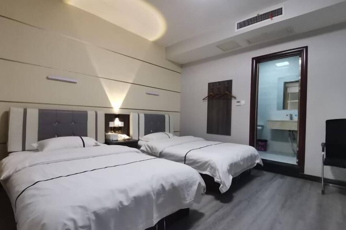 A hotel room with two beds, a bedside table with a lamp, a mirror, and a bathroom visible through an open door.