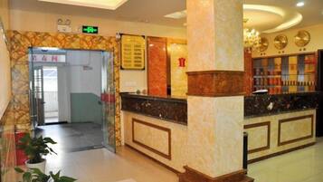 A hotel lobby with a reception desk, a glass door entrance, and a reception area with a marble column.